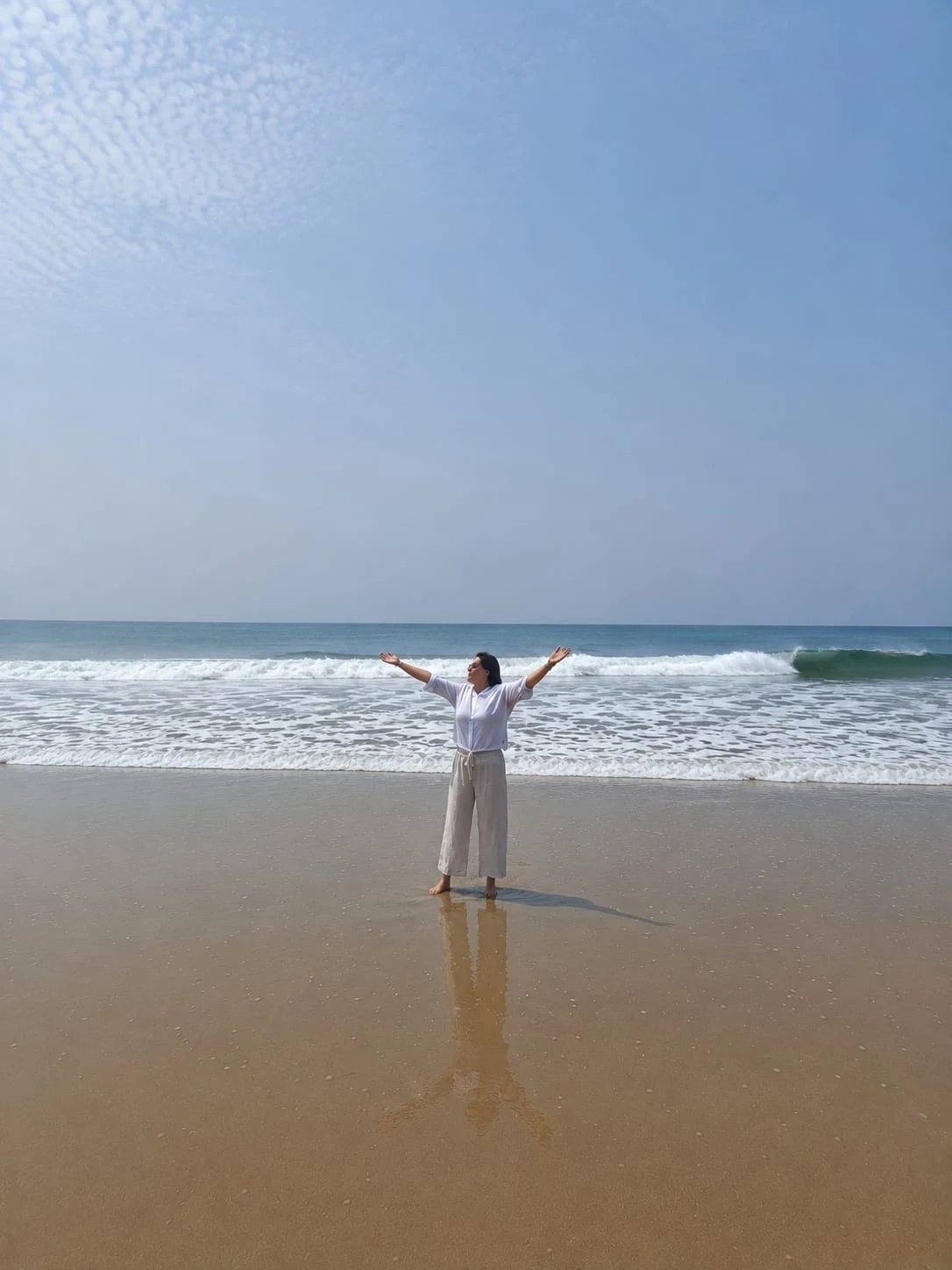 Personne vêtue de blanc face à la mer, les bras ouverts.